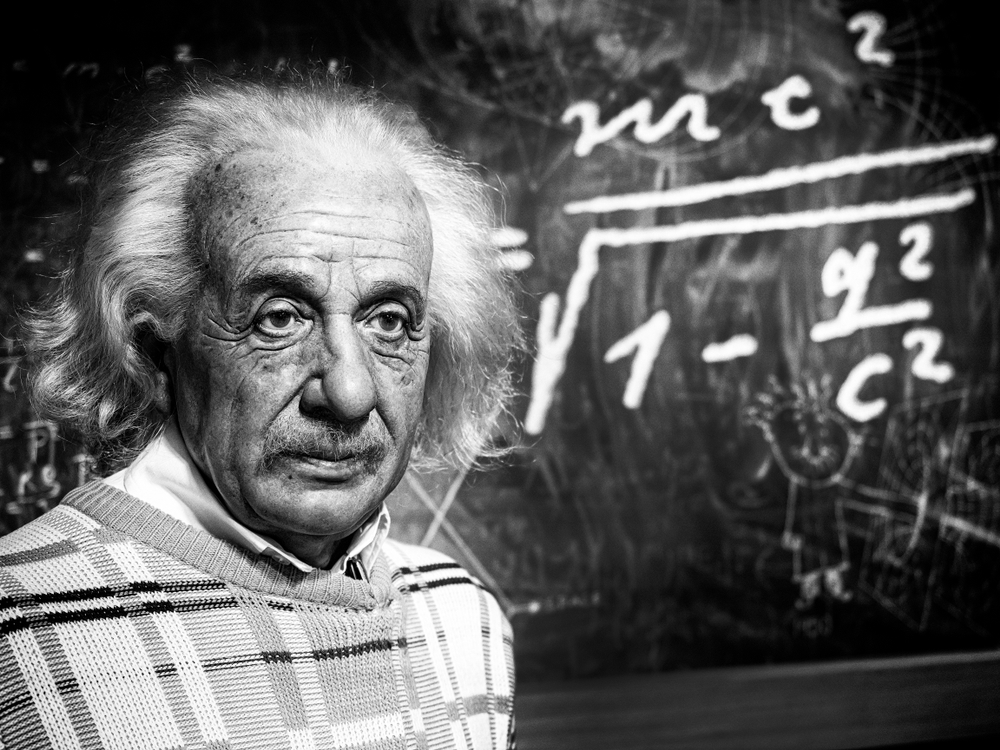 Albert Einstein with his famous formula partially behind him.